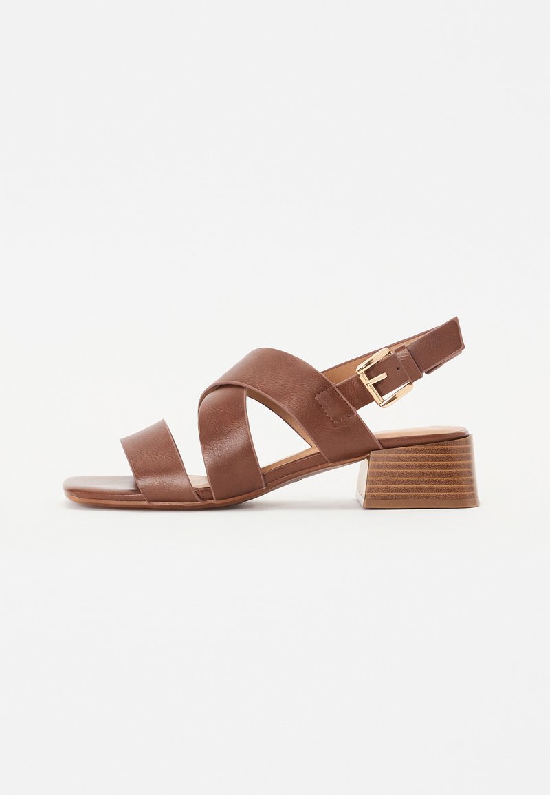 Sandal de couro castanho com design de tiras cruzadas, fivela ajustável no tornozelo e um salto bloco baixo empilhado com acabamento texturizado.