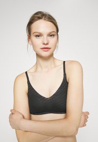Black bralette with a v-neck design, made from textured fabric featuring subtle wave patterns. Adjustable straps complete the look.