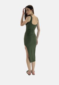 Abito senza maniche verde oliva con schiena bassa, silhouette aderente e spacco laterale. Tessuto morbido con superficie liscia e dettagli minimi.