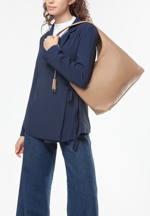 Beige leren hobo-tas met een ronde vorm, een soepele textuur en een lange schouderriem. Voorzien van een ritssluiting en een subtiele logodetail.