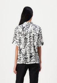 Chemise à manches courtes en tissu léger présentant un motif abstrait noir et blanc, avec un col pointu et une coupe décontractée.