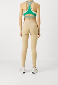 Sport-BH i grönt och grått med utskärning, matchad med beige leggings. Båda tillverkade av elastiskt material; leggingsen har dragkedjor vid anklarna.
