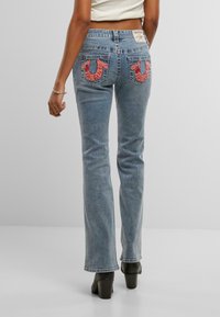Podložene jeans hlače v svetloblu prozoru z bledim teksturiranjem. Roza vezeni zadnji žepi predstavljajo edinstven dizajn. Dodelano z običajnim pasom.