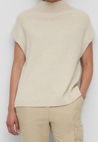 Pull en tricot beige avec un col montant, des manches courtes et des accents côtelés au niveau de l'encolure et de l'ourlet. Texture lisse et coupe décontractée.