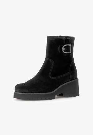 Bottines en suede noir avec un bout arrondi, un talon épais, un accent de boucle en argent et une couture contrastante sur les côtés. Semelle en caoutchouc texturée.
