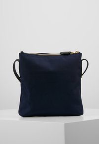 Borsa a tracolla in nylon blu navy con zip dorata, due manici in pelle nera e forma quadrata. Texture liscia, design minimalista.