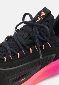 Scarpa sportiva nera con una tomaia texturizzata, dettagli rosa nella suola e lacci neri. Include accessori con marchio e un design unico.