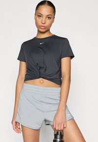 Κοντομάνικο t-shirt Nike σε σκούρο γκρι με λεπτομέρεια στριψίματος μπροστά· συνδυασμένο με αθλητικό σορτς ανοιχτού γκρι, παρουσιάζοντας έναν κομψό, αθλητικό σχεδιασμό.