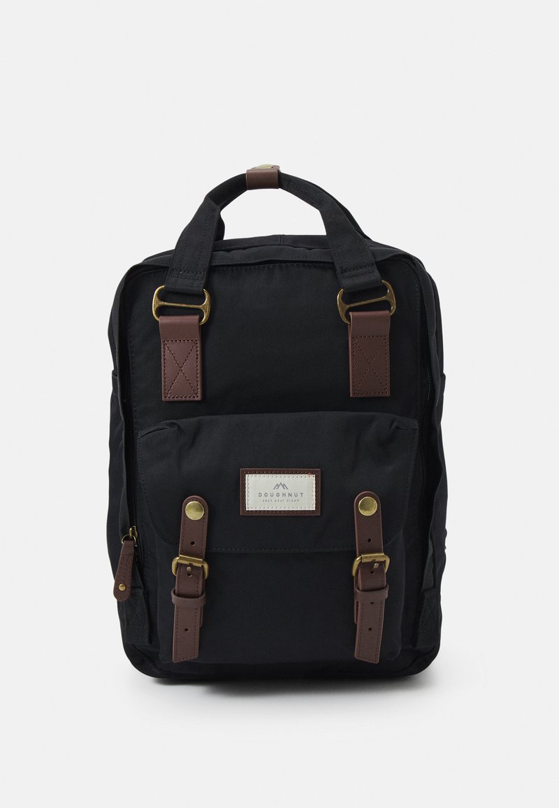 Sac à dos noir en tissu durable avec des accents en cuir marron, poches avant et bretelles ajustables. Présente une étiquette de marque sur le devant.