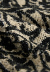Close-up of textured beige fabric with soft, black raised patterns resembling abstract or animal print designs.