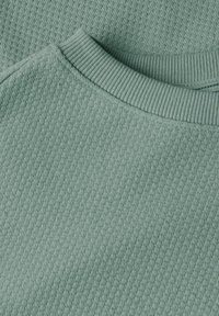 Jasno zielony sweter z fakturą, z prążkowanym kołnierzem i subtelnym wzorem w diamenty. Miękka tkanina zbliżenie na dekolt i obszar ramion.