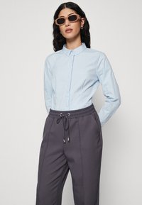 Chemise bleu clair à col classique, associée à un pantalon de survêtement gris foncé avec une taille élastique et un cordon de serrage.