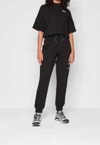 Sweatshirt noir court en tissu texturé associé à un pantalon taille ajustée assorti. Détails de baskets argentées et ceinture réglable.