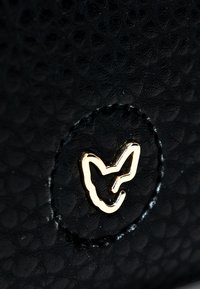 Pelle nera testurizzata con una toppa circolare che presenta un design del logo di una volpe dorata. La superficie mostra un motivo di piccoli diamanti in rilievo.
