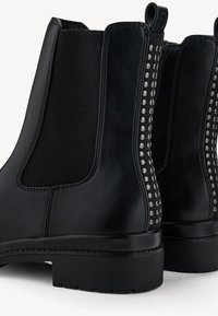 Svarta läderankle boots med elastiska sidopaneler, prydda med silvernitar längs de yttre kanterna och en låg gummisula.