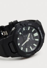 Montre G-SHOCK noire au design robuste, dotée d'un bracelet en silicone texturé, de marqueurs d'heure lumineux et de plusieurs boutons de fonction sur le côté.