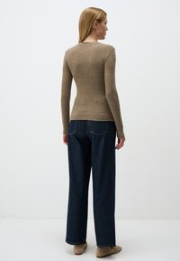 Top marrone a maniche lunghe attillato con scollatura a girocollo, abbinato a jeans in denim blu a gamba larga e vita alta, mostrato da dietro.