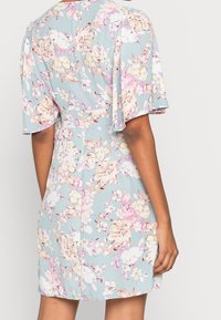 Květinové šaty v světle modré barvě, s krátkými plandavými rukávy, se staženým pasem a barevným potiskem růžových a bílých květin po celém povrchu.