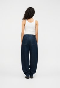 Σκούρο μπλε τζιν παντελόνι με φαρδιά μπατζάκια και ψηλή μέση, με πίσω τσέπες και απαλή υφή, συνδυασμένο με λευκό αμάνικο τοπ.