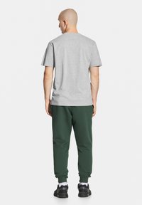 Szara koszulka z krótkim rękawem i ciemnozielone spodnie dresowe. Materiał wydaje się miękki, o luźnym kroju. Noszone są trampki z białymi akcentami.