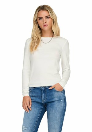 Weißes Langarmshirt mit rundem Ausschnitt, aus weichem Material gefertigt, kombiniert mit hellblauen, ausgewaschenen Denim-Jeans. Schlichtes Design, keine sichtbaren Muster.