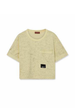 Krótki t-shirt w jasnobeżowym kolorze z krótkim rękawem, o subtelnym cętkowanym wzorze, z okrągłym dekoltem, kieszenią z przodu oraz czarną naszywką "HEY" na kieszeni.