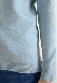 Jasnoniebieski sweter z miękkiego, teksturowanego materiału. Posiada prążkowane mankiety i dół, z lekko dopasowanym krojem. Widoczny materiał dżinsowy poniżej.