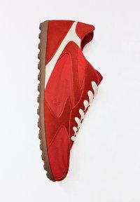 Basket en daim et cuir rouge avec lacets blancs, semelle en caoutchouc marron et détail d'une bande blanche sur le côté sur fond uni.