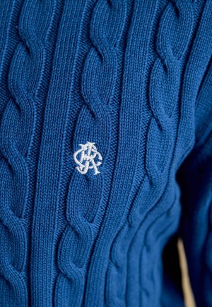 Pull bleu en maille torsadée avec les lettres entrelacées "J" et "R" brodées en blanc sur la poitrine.