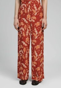 Pantalons à jambe large en rouille avec un imprimé floral et paisley en orange et blanc. Comprend une fermeture à bouton et un tissu texturé.