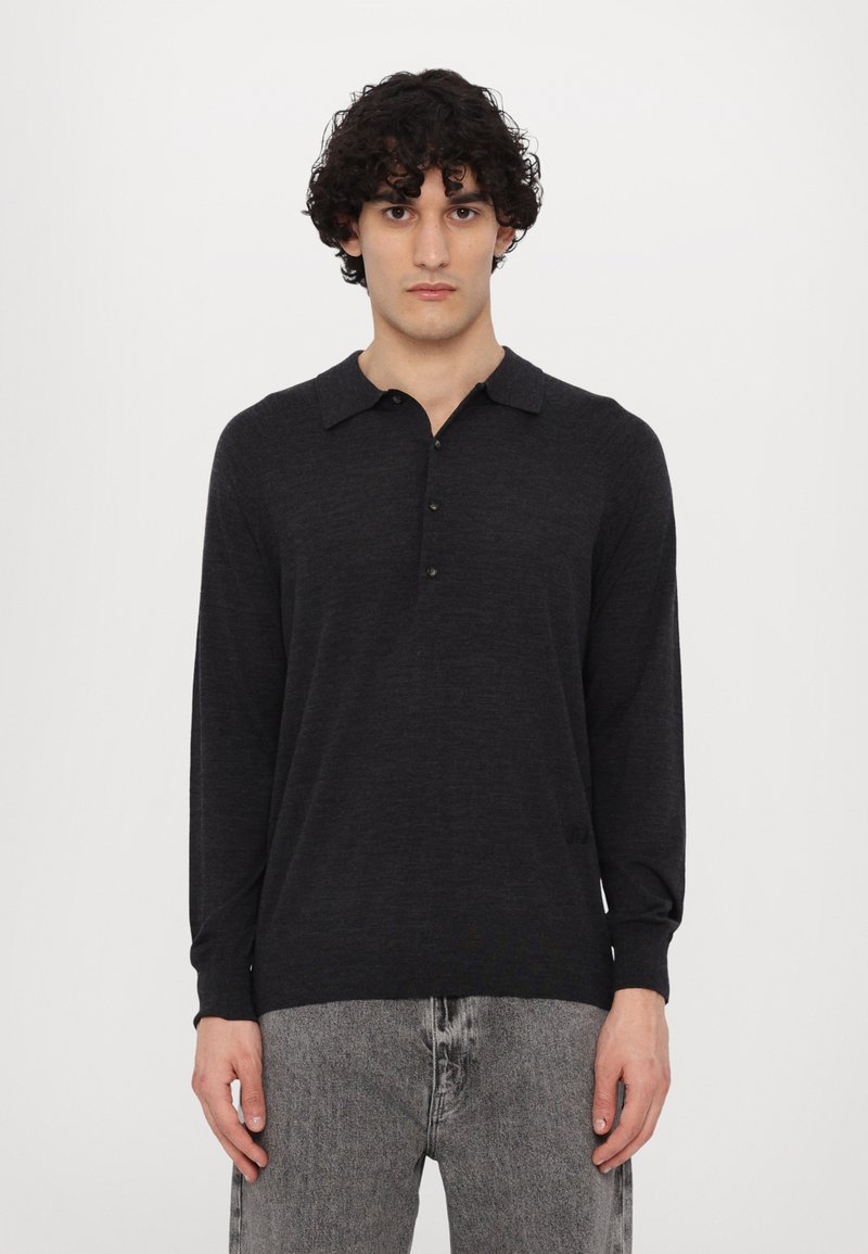 Polo noir à manches longues avec col, patte de boutonnage et poignets côtelés, associé à un jean gris déchiré. Texture douce, design décontracté.