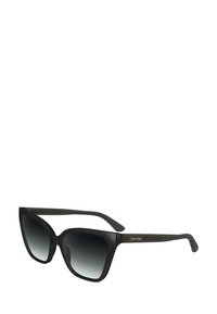 Occhiali da sole oversized neri con lenti a gradiente da scuro a chiaro, caratterizzati da una forma geometrica a occhio di gatto e dal marchio Calvin Klein sul lato.
