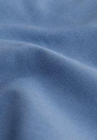 Svetlo modra tkanina z gladko teksturo, ki ima fino diagonalno rebrasto vzorec, prikazuje gube in mehki sijaj.