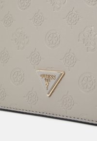 Materiale grigio goffrato con un motivo ripetitivo del logo, con un accento hardware triangolare dorato che presenta la scritta "GUESS USA".