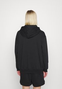 Svart, oversized hoodie med ficka fram, ribbade mudd och nederkant. Bärs med matchande svarta shorts av fintexturerat tyg.