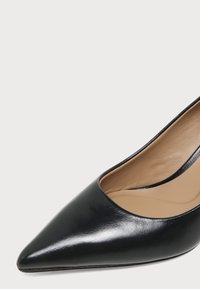 Escarpin femme en cuir noir à bout pointu avec une doublure intérieure beige lisse, présenté sur un fond gris clair uni.