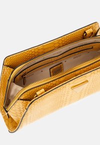 Borsa gialla in tessuto texturizzato con motivo rettile, scomparti con zip e un interno beige con accenti del logo del marchio.