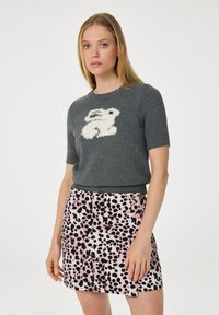 Grijze gebreide trui met korte mouwen, versierd met een ontwerp van een witte pluizige konijn, gecombineerd met een roze rok met zwarte en roze spetterpatronen.