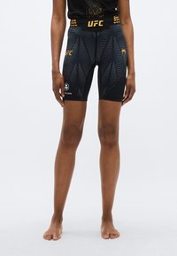 Shorts UFC noirs avec un motif texturé de feuilles, des accents jaunes, et une taille haute. Conviennent à une utilisation athlétique.