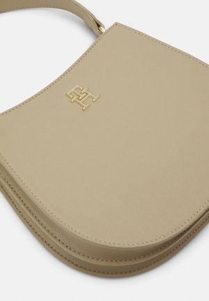 Sac à main en cuir beige avec un logo géométrique doré sur le devant, des coutures visibles et une vue partielle de la poignée.