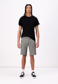 Tricou negru cu mânecă scurtă, pantaloni scurți gri până la genunchi și teniși negri cu talpă albă. Stil casual, design minim și textură ușoară.