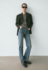 Zwarte blazer, gestreept shirt, blauwe jeans met rechte pijpen en donkere instappers. Accessoires zijn onder meer zwarte zonnebril en een lange hangerketting.