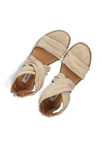 Beige suede sandals with an open toe, wrapped straps, and a brown leather heel. Fastened with a silver-tone buckle detail on the side.