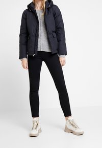 Granatowa kurtka puchowa z kapturem, szary sweter dzianinowy, czarne dżinsy skinny i beżowe botki za kostkę z teksturowaną podeszwą.