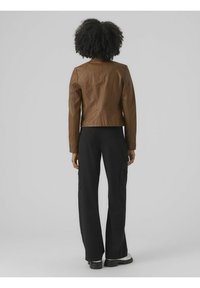 Giubbotto in pelle marrone dal design aderente, con colletto alto e dettagli senza cuciture. Abbinato a pantaloni cargo larghi neri e stivali chunky.