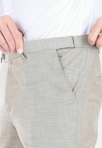 Pantaloni grigi chiari, testurizzati e dal taglio slim, con tasche laterali e fronte piatto, abbinati a una camicia bianca.