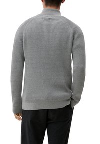 Homme portant un pull gris côtelé à manches longues avec un col montant et un pantalon noir, vu de dos.