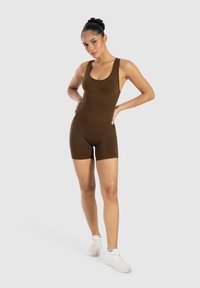 Brun bodysuit med rundad halsringning, breda axelband och en åtsittande design, parat med vita sportskor på en neutral bakgrund.
