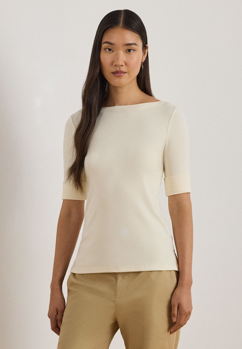 Cream, fitted top with short sleeves and a straight neckline. Soft texture with side slits. Paired with light beige pants.