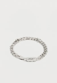 Βραχιόλι με αλυσίδα σε ασημί τόνο, με κούμπωμα αστακού και ορθογώνια πινακίδα σκαλισμένη με μια στυλιζαρισμέν η υπογραφή.